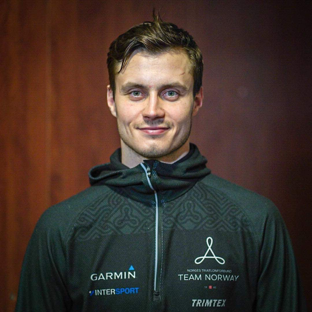 Smilende mann i svart treningsjakke med Team Norway-logo foran mørk bakgrunn.