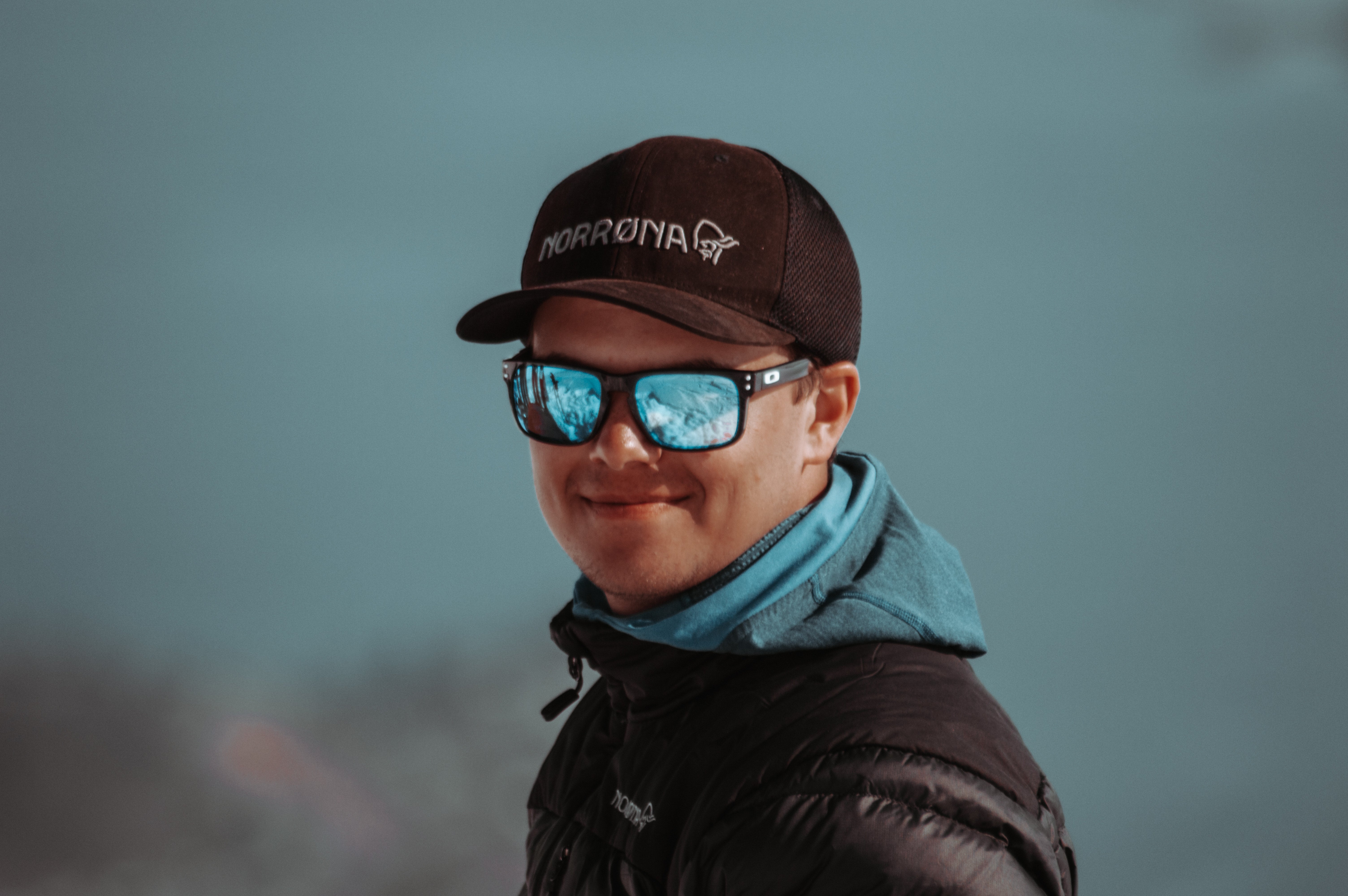 Smilende mann med caps og solbriller, iført turklær, ute i frisk fjellnatur.