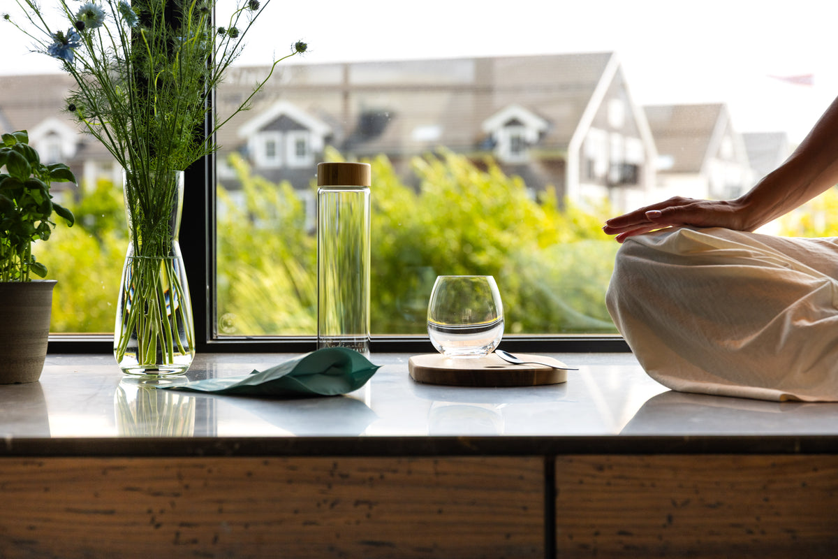 Vannflaske fra Radiant Health på vinduskarm med planter – renhet og balanse.