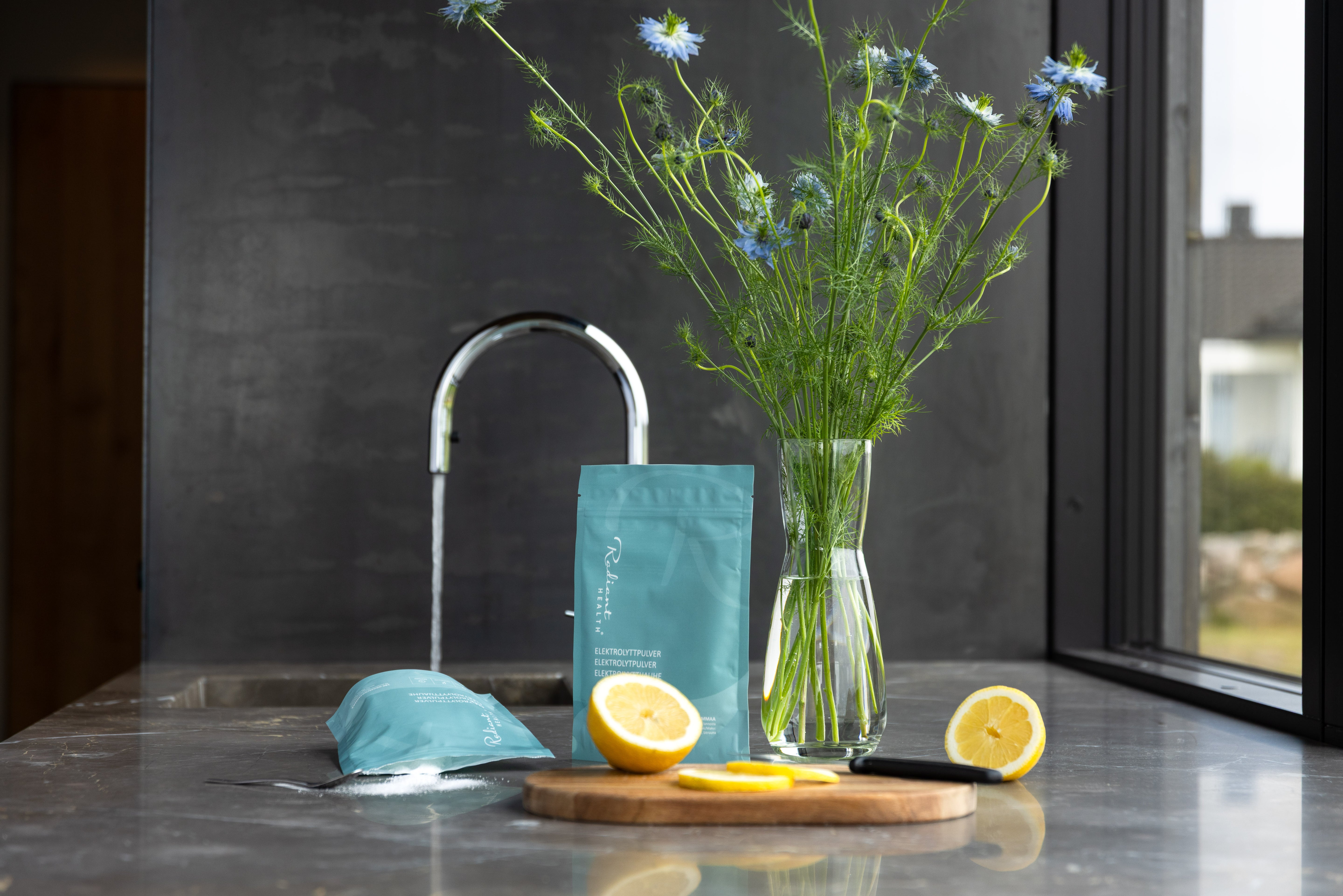 Elektrolyttpulver fra Radiant Health på kjøkkenbenk med sitron og vann – naturlig hydrering og mineralbalanse for daglig velvære